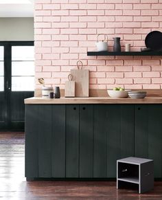 a kitchen with black cabinets and pink brick wall behind the countertop is filled with dishes