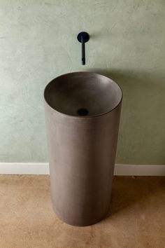 a round concrete sink in front of a green wall with a black faucet