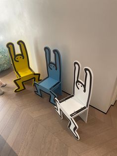 three colorful chairs sitting next to each other on top of a hard wood floor in front of a white wall