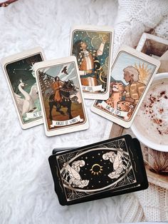 four tarot cards sitting on top of a table next to a cup of coffee