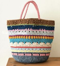 a multicolored crocheted bag sitting on top of a wooden table next to a white wall