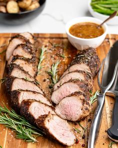 sliced meat on cutting board with knife and fork next to bowl of dipping sauces