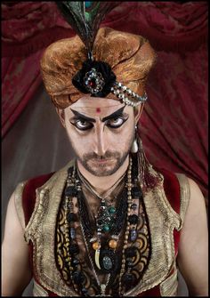 a man with makeup and feathers on his head is dressed in an elaborately designed costume