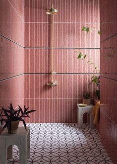 a bathroom with pink tiles and plants in the corner, along with a white stool