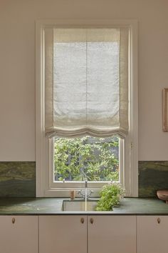 a kitchen with white cabinets and green counter tops next to a window that has roman shades on it