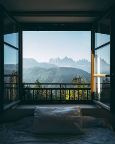 a bed sitting in the middle of a bedroom next to a window with mountains outside