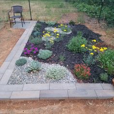 a garden with flowers and rocks in the ground next to a chair on a patio