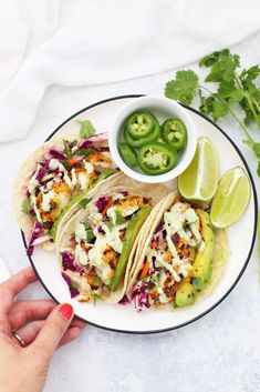 three tacos on a plate with limes and jalapenos next to them