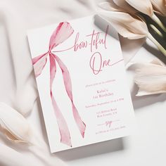 a pink and white bow - tied birthday party card on a bed with tulips