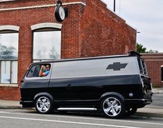 a black van parked in front of a brick building with a clock on it's side