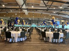 a banquet hall with tables and chairs set up for a formal function, decorated with blue and gold balloons