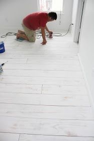 a man in red shirt and tan shorts working on white flooring with paint rollers