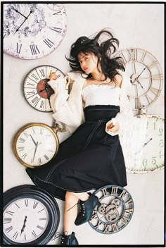 a woman laying on the ground next to several clocks and clock faces with her hair blowing in the wind