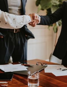 two people shaking hands at a table with papers and glasses on it, one holding the other's hand