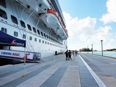 people are walking on the sidewalk next to a large cruise ship in the water with blue sky and clouds