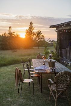 a wooden table with chairs and plates on it in front of a barn at sunset