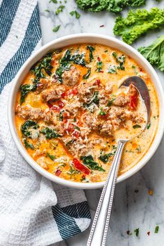 a bowl of soup with meat and spinach on the side next to a spoon