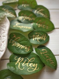 green leaves with gold writing on them are laying next to a white bowl and lace doily