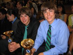 two young men sitting next to each other holding trophies