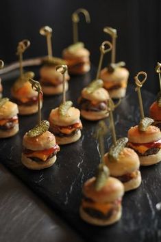 mini burgers with toothpicks are arranged on a black plate