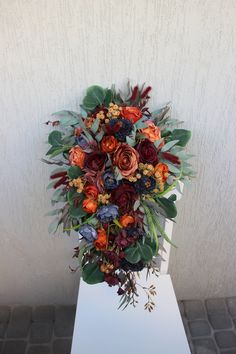 a bouquet of flowers is sitting on top of a white stand with leaves and foliage