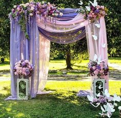 an outdoor wedding setup with purple and white flowers on the arbor, butterfly decorations, and lanterns