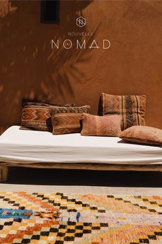 a bed sitting in front of a brown wall with pillows on top of it next to a rug