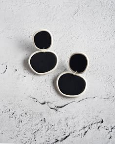 two black and white oval shaped earrings sitting on top of a cement surface with one earring in the shape of an oval