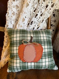 an orange patchwork pumpkin pillow on a green checkered pillow cover with a white lace doily