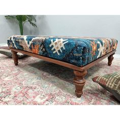 a blue and orange ottoman sitting on top of a rug next to two pillows in front of a potted plant