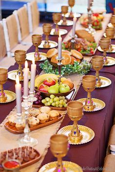 a long table is set with plates, candles and fruit for a festive dinner