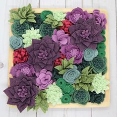 felt flowers are laid out on a wooden board with green leaves and purples in the center