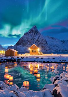 some lights floating in the water next to a mountain and snow covered ground with houses