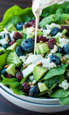 a salad with blueberries, avocado and spinach is being drizzled with dressing