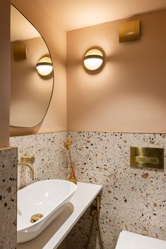 a white sink sitting under two round lights in a bathroom next to a toilet and mirror