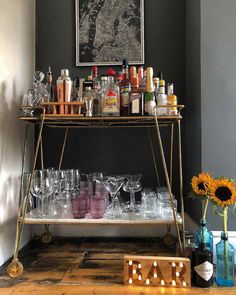 a bar cart filled with wine glasses and bottles on top of a wooden floor next to a wall