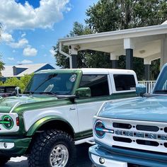 two green and white ford trucks parked in front of a house with palm trees behind them