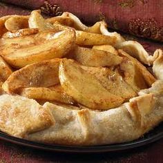 an apple pie on a black plate with apples in the background and a red table cloth