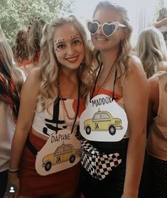 two women in costumes pose for the camera at a car themed party with other people