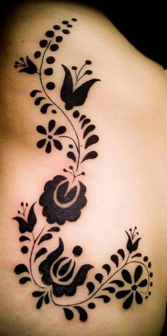 a woman's back tattoo with black flowers and leaves on the side of her stomach