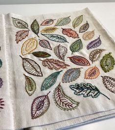 two napkins with embroidered leaves on them sitting next to each other in front of a white counter