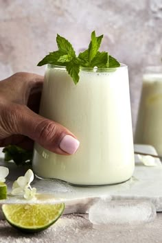 a hand is holding a glass filled with milk and garnished with mint