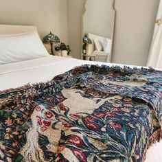 a bed with a blanket on top of it next to a mirror and window sill