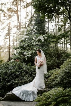 a woman in a wedding dress is standing on a stone path and holding a bouquet