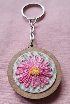 a pink and white flower on a wooden circle keychain hanging from a hook