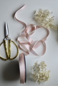 some flowers and scissors on a table with pink satin ribbons next to them, along with a pair of scissors