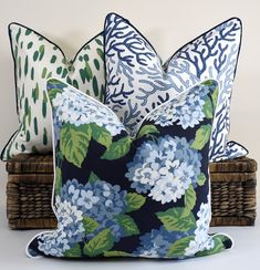 three pillows with blue and green flowers on them sitting next to each other in front of a wicker basket