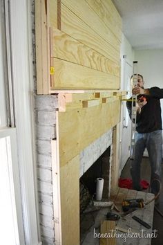 a man standing next to a fire place in a living room under construction with wood planks on the wall