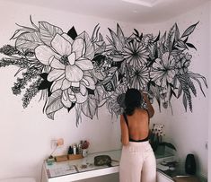 a woman standing in front of a wall with flowers painted on it