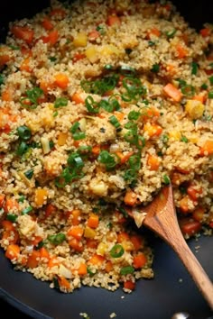 a pan filled with rice and vegetables on top of a wooden spatula next to a wooden spoon